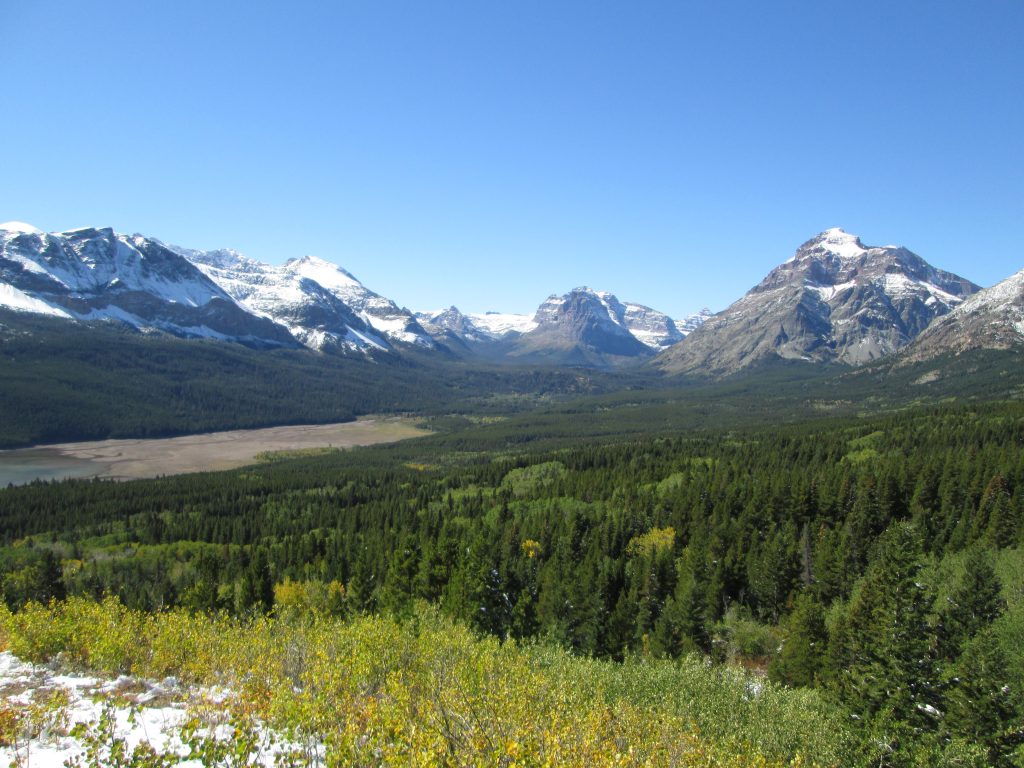 A green, sun-bathed valley surrounded in the distance by peaks of the Rocky Mountain range. An illustration of the rest and relaxation the author is enjoying through financial independence. 